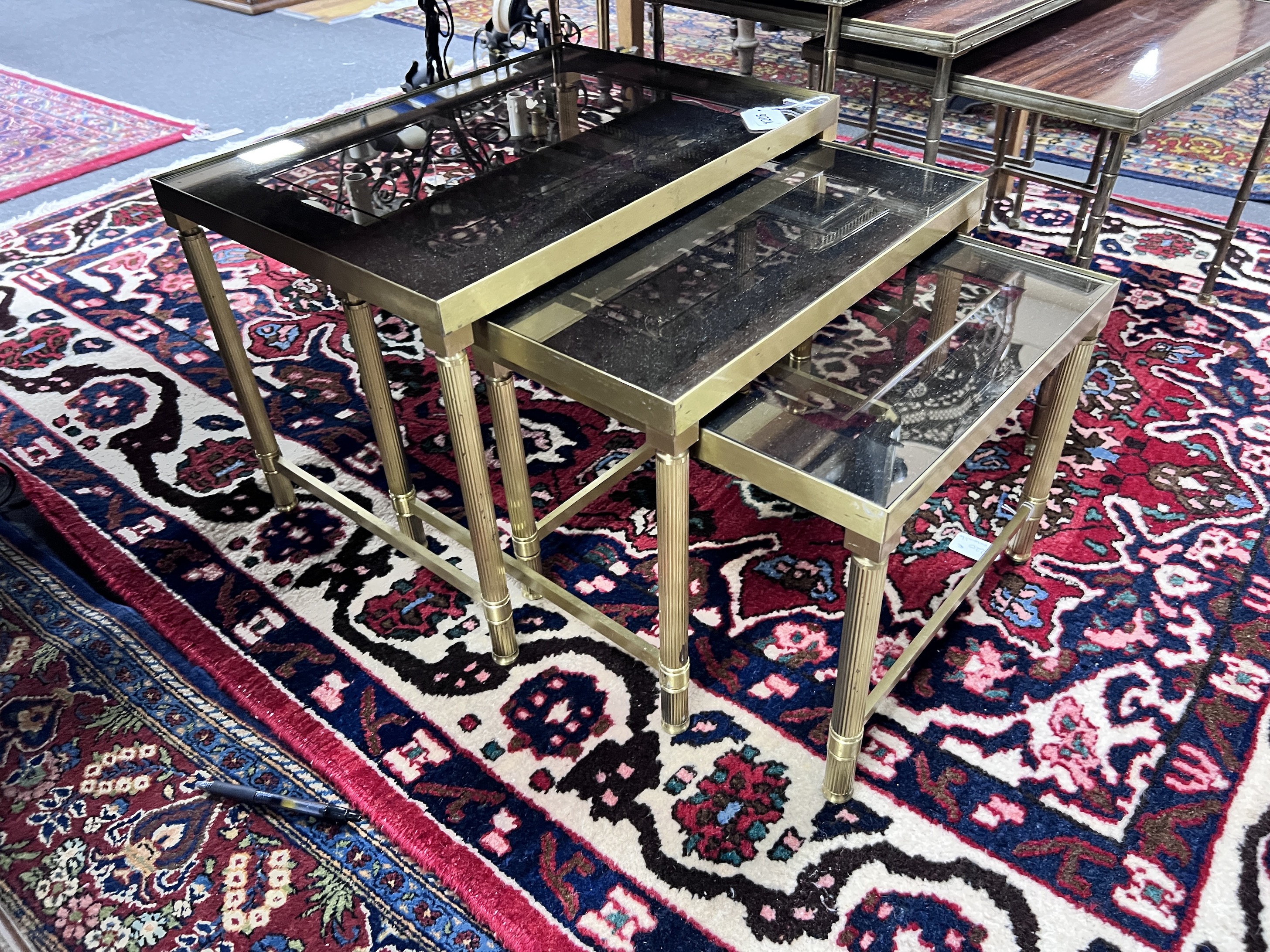 A nest of three 'Maison Charles' style brass and smoked glass topped tables, largest width 50cm
